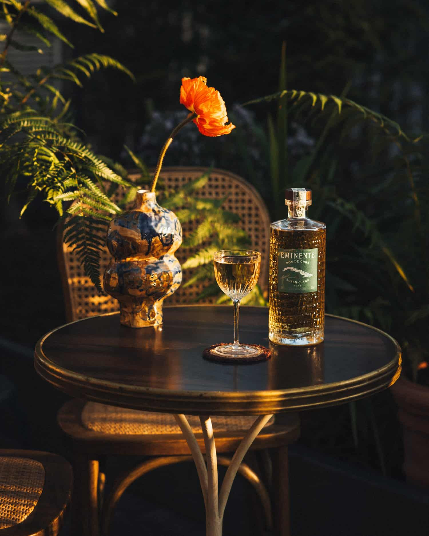 Mesa con un florero, una copa, y el ron propio de Eminente en Drawing Hotel 